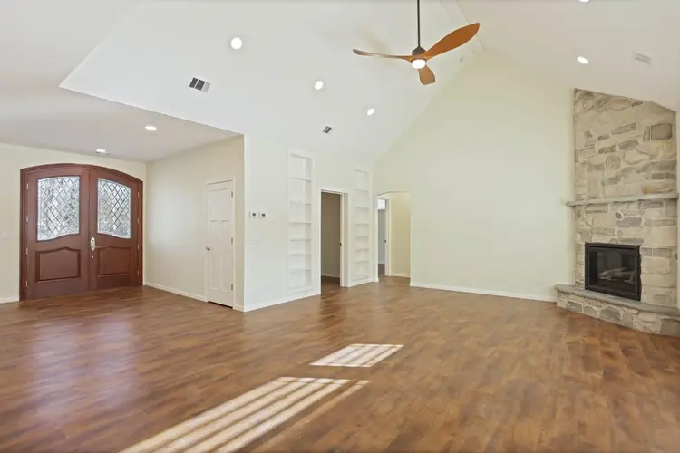 Modern living room with vaulted ceiling, stone fireplace, hardwood floors, and built-in shelves